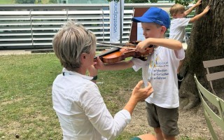 Eine Frau unterrichtet einen Jungen beim Spielen einer Geige im Freien.