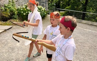 Ein Junge mit blauem T-Shirt und Jeans hält einen einfachen Pfeilbogen. Er trägt eine rote Nase.