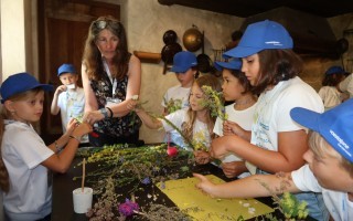 Kinder basteln mit Blüten und Blättern. Eine Frau zeigt ihnen eine Technik.