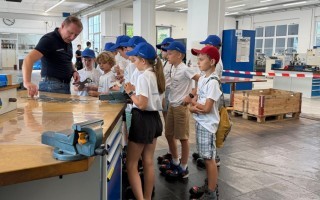 Schulkinder beobachten einen Lehrer am Arbeitsplatz, bei der Anleitung eines Werkzeugs.