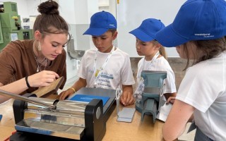 Ein Mädchen erklärt einem Schüler die Konstruktion eines kleinen Modells mit einem Messer und einer Schablone.