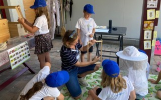 Kinder an einer Malwerkbank, eine Frau beobachtet sie, Bilder von Insekten an der Wand.