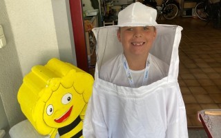 Person in Schutzkleidung vor einer gelben Bienenfigur im Hintergrund.