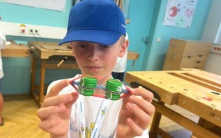 Junge hält zusammengefaltete Plastikflaschen in den Händen. Im Hintergrund ein grüner Klassenzimmer.