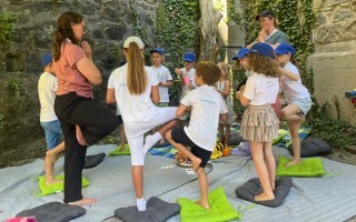 Kinder üben Yoga auf einer Matte im Freien.