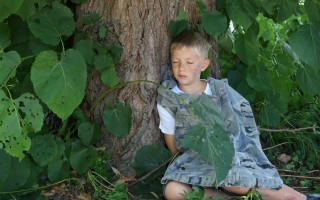 Ein kleiner Junge sitzt an einem Baum, umgeben von großen Blättern.