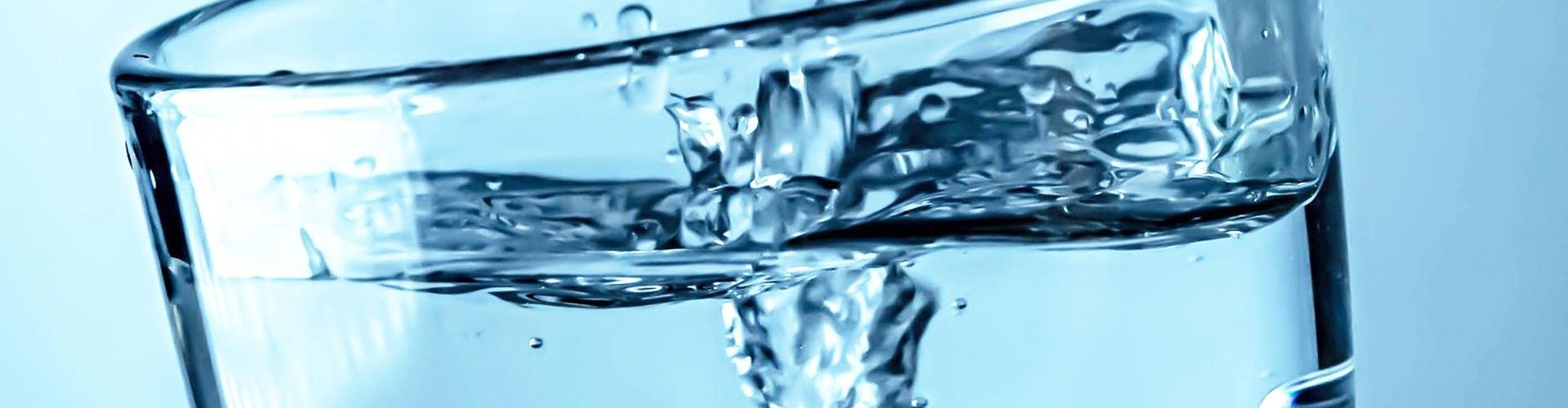 Ein Glas mit fließendem Wasser, das in einem Wirbel zu einem Strömen überläuft.