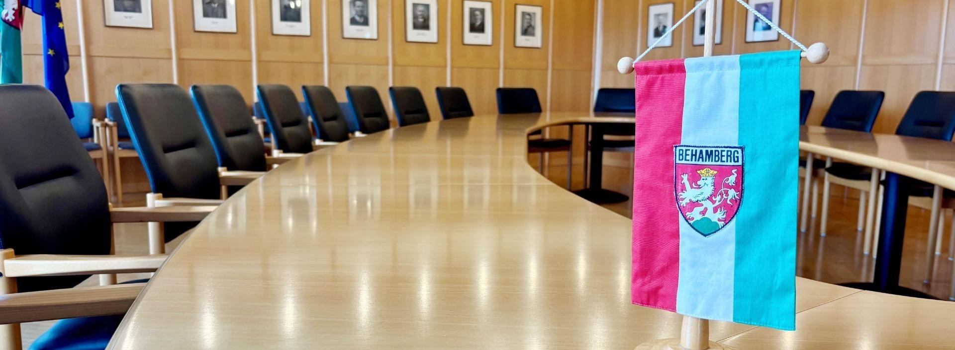 Tischkonferenzraum mit langen, schlichten Tischen und Stühlen. Ein blau-weißes Banner mit Wappen auf dem Tisch.
