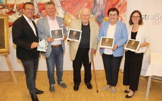 Fünf Personen stehen vor einem Hintergrund mit einem Bild von Johann Reichert.