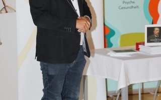 Mann in Anzug vor Hintergrundwand bei einer Ausstellung.