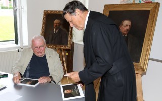 Alter Mann unterschreibt Portrait eines Mannes vor einem goldenen Rahmen.