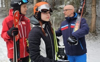 Drei Skifahrer in Schneemantel und Skibrille stehen am Rande eines skizigen Weges und blicken in die Ferne.