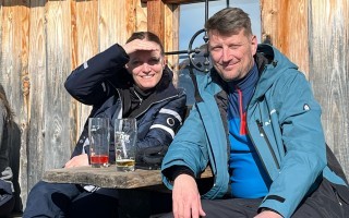 Zwei Personen in blauen Regenjacken sitzen an einem Tisch und halten Biergläser in der Hand.