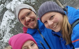 Drei Personen im Schnee, gefangen in einem Lächeln. Eine Frau in blau, eine in pink und ein Mann mit grauem Schal und Brille.