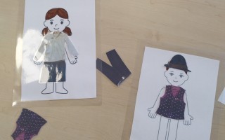 Zwei Personen-Vorlagen auf einem hellbraunen Tisch. Eine zeigt ein Mädchen in blauem Kleid, die andere ein Junge im schwarzen Anzug.