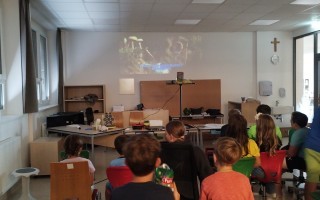 Schulklasse mit Kindern, die auf einen Lehrer oder eine Lehrkraft hören, in einem Klassenzimmer mit Schreibtischen und Bürostühlen.