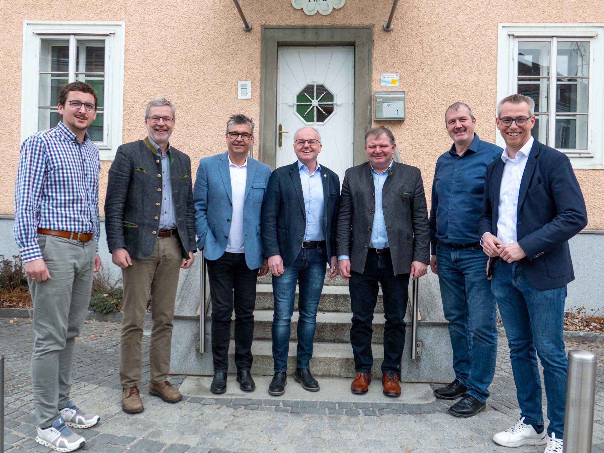 Sechs Männer stehen vor einem Gebäude. Sie tragen verschiedene Anzüge und Schuhe.