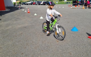 Kind lernt Fahrradfahren auf asphaltierter Fläche mit Gelbwesten und Markierungen.