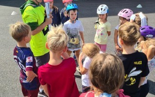 Kinder mit Helm umrunden einen Erwachsenen auf einem Schulhof.
