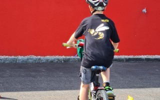 Ein Junge fährt Fahrrad. Er trägt einen Helm und Sicherheitskleidung. Zwei gelbe Warncones stehen im Hintergrund.