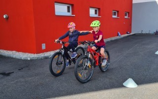 Zwei Kinder fahren gemeinsam Fahrrad auf einer Straße.