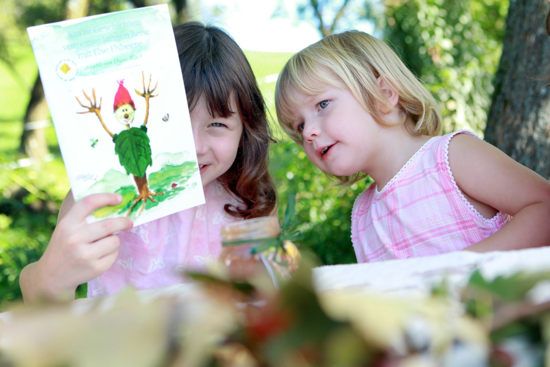 Zwei Kinder betrachten gemeinsam ein Bild mit einem kleinen Kobold im Grünen.