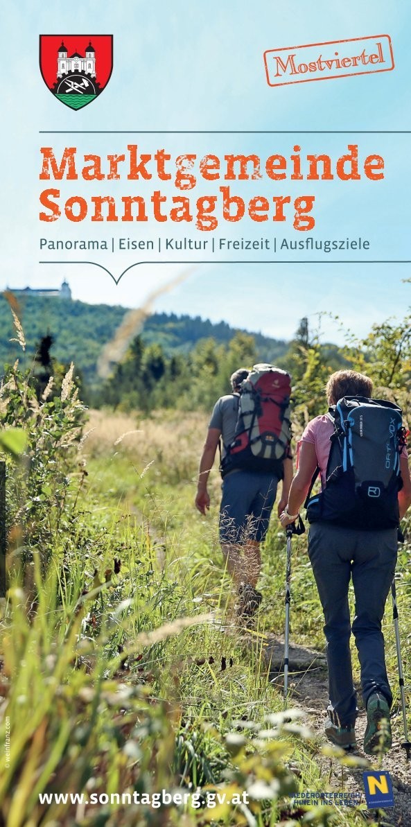 Zwei Wanderer mit Rucksäcken durchziehen eine Bergwiese im Sonnenberg.