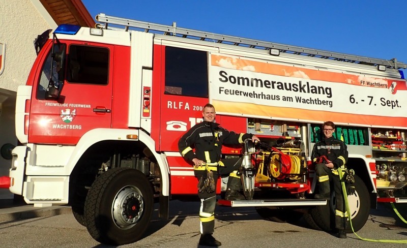 Feuerwehrfahrzeug am Wachsberg. Zwei Feuerwehrleute stehen neben einem roten Mannschaftsfahrzeug mit dem Schriftzug 