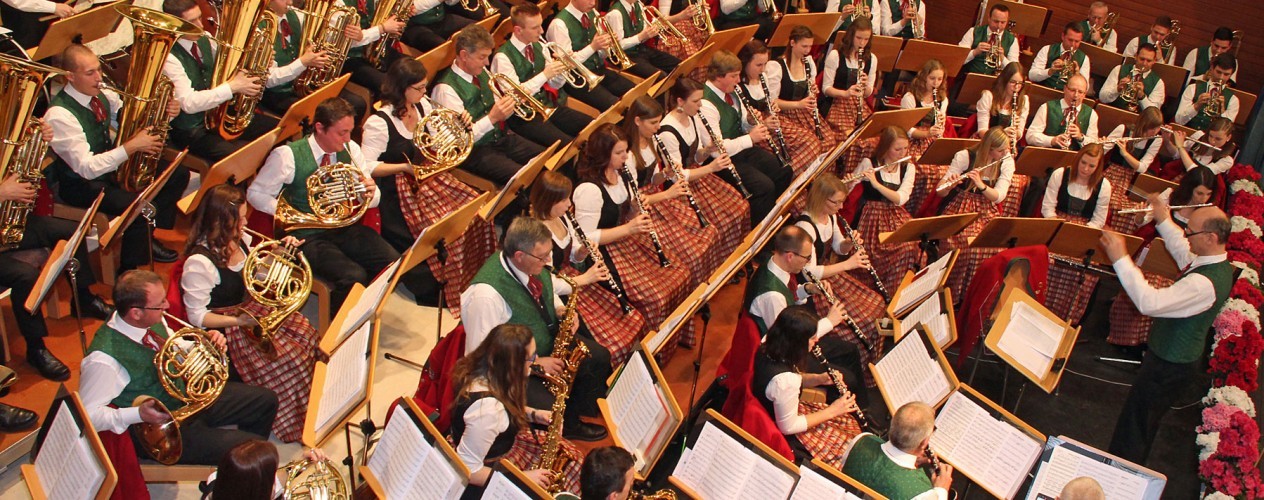 Ein großes Orchester mit vielen Musikern in grünen und roten Schottenmuster-Shirts spielt zusammen auf einer Bühne.