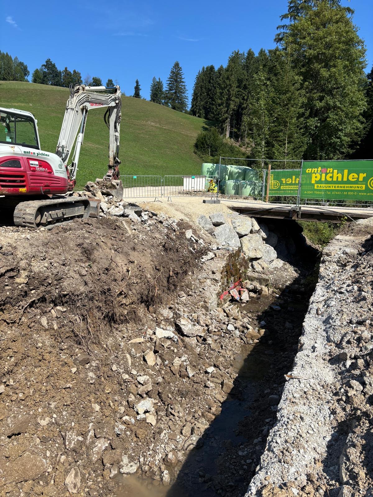 Bagger Anton Pichler arbeitet an einer Baustelle mit Brücke und Bachbett in Österreich.