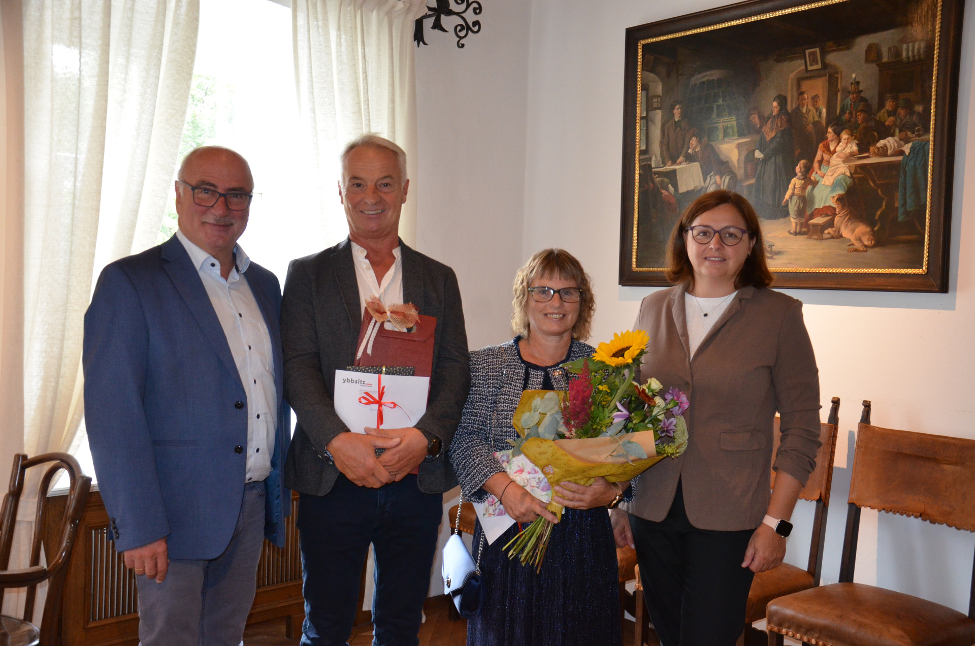 Vier Personen mit Geschenken und Blumen vor einem Gemälde in Österreich