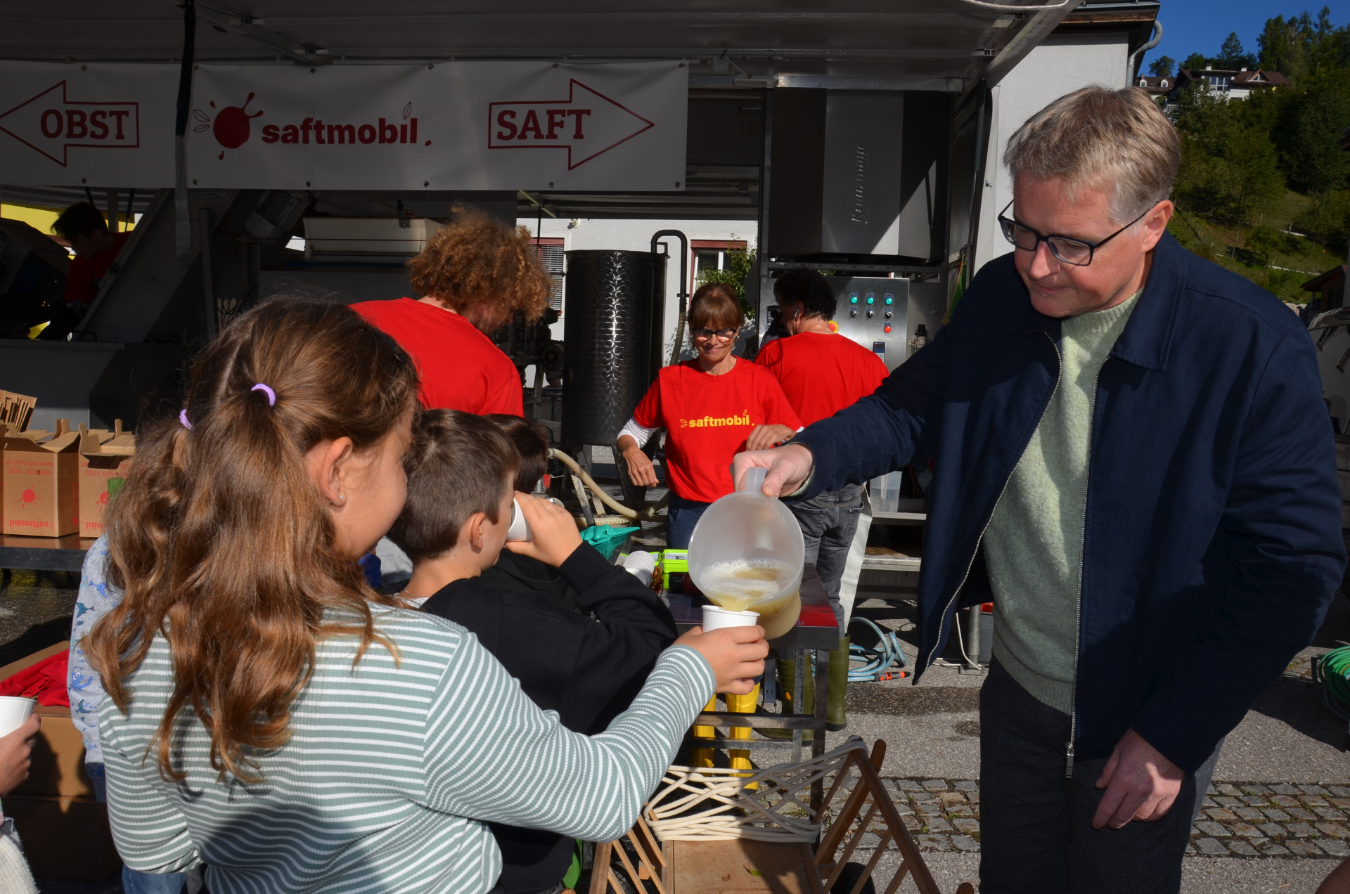 Saftmobil-Mitarbeiter gießt Saft in ein Glas für Kinder vor einem Stand in Österreich.